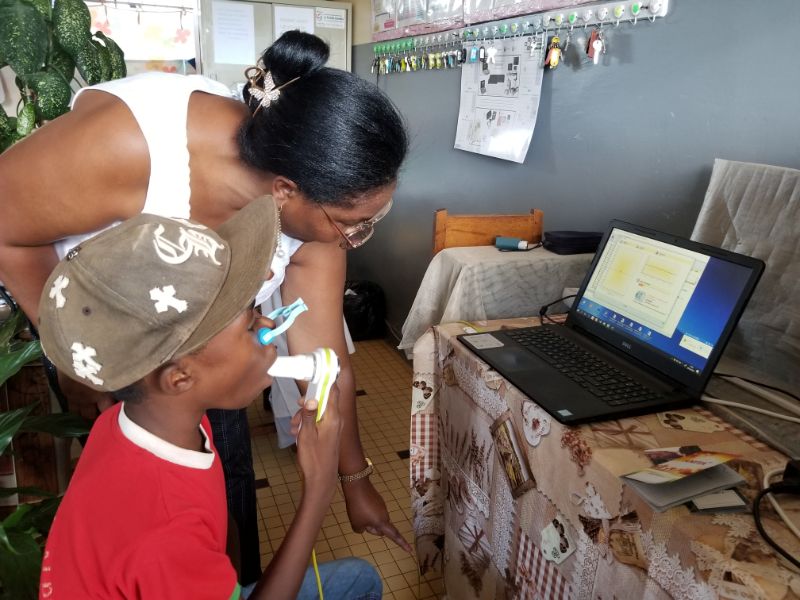 A female doctor guides a 14-year-old boy in breathing out into a device for an asthma test.