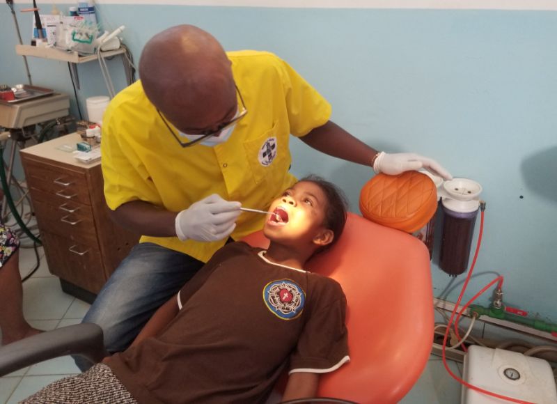 A middle-aged man examines a young girl's teeth at a dental office.