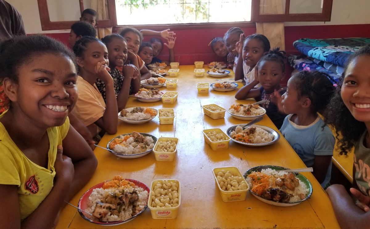 a large group of girls smile for a photo before eating their meals