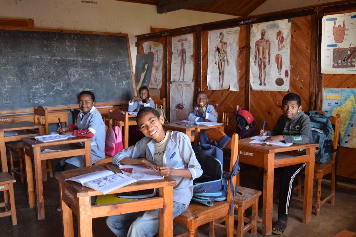 students smiling for a photo while sitting at their desks in a classroom