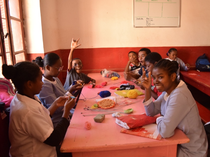 A dozen students ranging in age from 14 to 24 practice crochet at a pink table in SEMAFI's dining room.