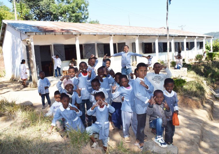 A group of roughly two dozen elementary school students pose for the camera in their uniforms in front of the school at SEMAFI.