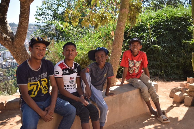 Four teenage boys, including Mandimby, sit on a concrete bench outside smiling for the camera.