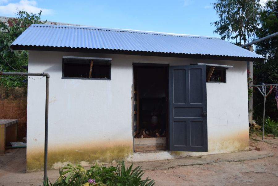 This image shows the new chicken house. It's a medium-sized masonry structure with a metal roof, measuring approximately 15 feet across and 10 feet tall. Two front windows are propped open with sticks for ventilation and the door is open, presumably because a staff member is inside caring for the chickens.